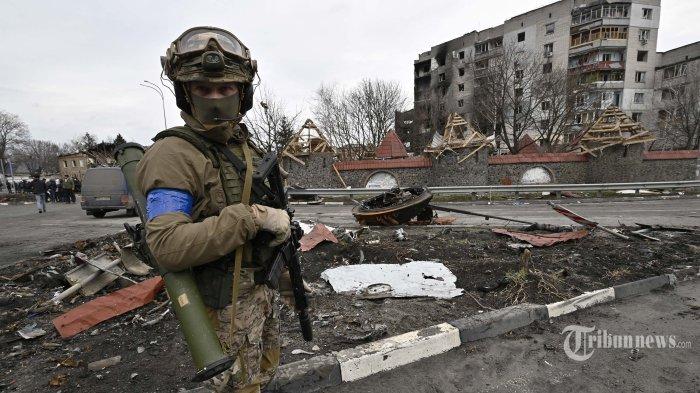 Seorang prajurit Ukraina berjaga di jalan di samping sebuah bangunan yang rusak di kota Borodianka, barat laut Kyiv, pada 6 April 2022, akibat terkena gempuran militer Rusia