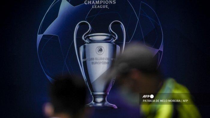Orang-orang berdiri di depan papan reklame yang menggambarkan trofi Liga Champions UEFA