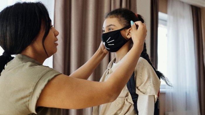 Orang tua membantu anak memakai masker sebelum berangkat ke sekolah