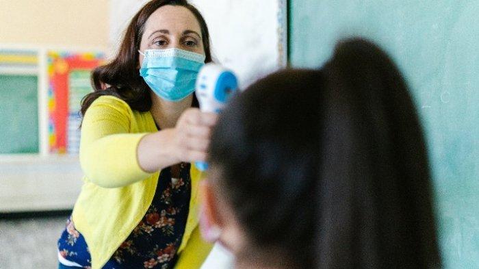 Guru melakukan cek suhu kepada anak sebelum masuk ke ruangan kelas.