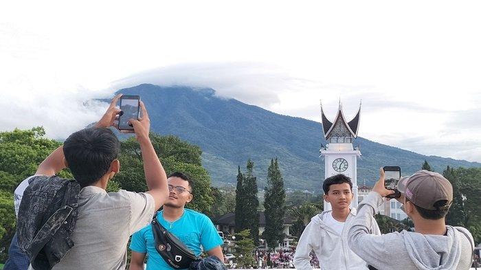 Tempat Wisata Sumatera Barat Jam Gadang-Dua orang wisatawan tengah memotret masing-masing temannya di rooftop Pasa Ateh (Pasar Atas) Kota Bukittinggi berlatar Jam Gadang dan Gunung Singgalang, Kamis (5/5/2022)