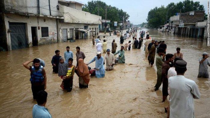 Pengungsi mengarungi daerah banjir di Peshawar, Khyber Pakhtunkhwa, Pakistan pada hari Sabtu (27/8/2022). (CNN Internasional)
